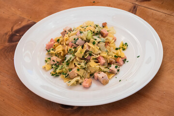 Krautfleckerl, Austrian pasta with caramelized cabbage with Roast Pork on a White Plate on a Rustic Wooden Table