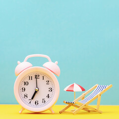 Alarm clock and toy deckchair with an umbrella from the sun on a colored background, concept of...