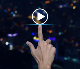 Hand pressing play button flat icon over blur colorful night light modern city tower and skyscraper, Business music online concept