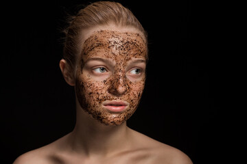 Fototapeta premium Skin scrub Coffee grounds mask on the face of a beautiful young woman Organic natural cosmetology dark studio background Isolate