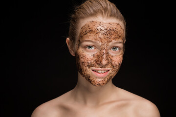 Skin scrub Coffee grounds mask on the face of a beautiful young woman Organic natural cosmetology dark studio background Isolate