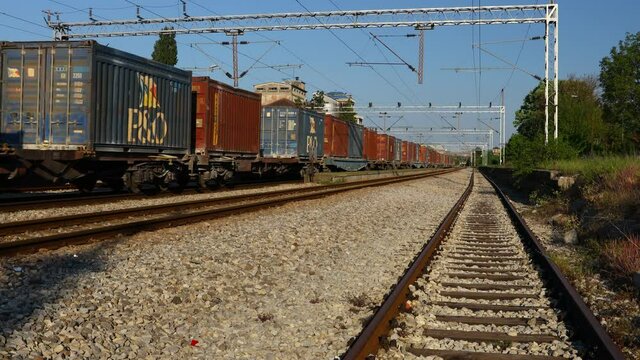 View on long composition, railway freight train of cargo shipping containers in passing through industrial rural place.
