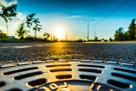 Sunset in the country, the empty highway. Wide angle view of a close up from the level of the sewer manhole on pavement