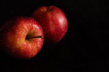Two ripe fresh red apples with water drops on glossy peel on black background
