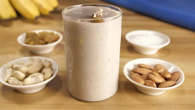 Vegan milk from nuts in a glass around various nuts on a wooden table - healthy protein drink. Almond  cashew nuts  raisins  ripe banana  and little sugar to make a nutritious milkshake - a healthf...