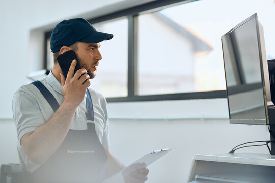 Car Mechanic Talking On The Phone While Using Computer At Auto Repair Shop.