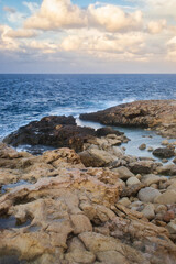 Fototapeta na wymiar Rocks leading out to the blue ocean water in Qawra, Malta on a fall evening.