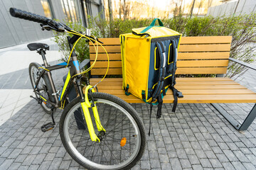 Obraz premium yellow thermal backpack and bicycle in the city. Food delivery service concept.