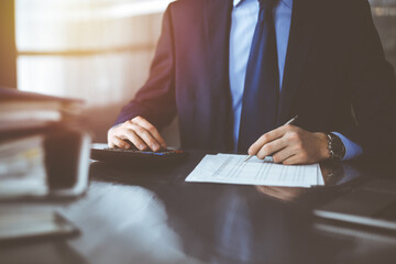 Unknown man accountant in blue blazer use calculator and computer while staying at home during covid pandemic. Taxes and audit