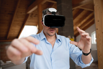 good looking male architect with virtual reality goggles and blue shirt on construction site in loft, attic
