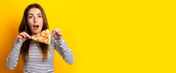 surprised young woman holding a slice of fresh pizza on a yellow background. Banner