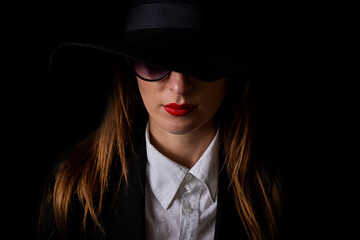 portrait of a beautiful young woman in a black hat and glasses on a black background