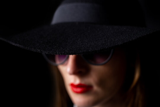 young woman in a black hat and glasses on a black background