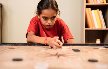 Front view of alone Young girl kid practicing or playing Carrom board at home - Concept of autism...