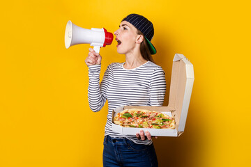 smiling young woman pizza delivery man shouting into a megaphone while holding pizza on yellow background