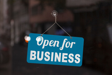 Close-up on a blue open sign in the window of a shop displaying the message: Open for business..