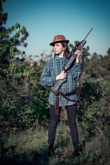 Fototapeta premium Portrait of a young beautiful girl hunter in a hat and with a hunting rifle in her hands, soft focus