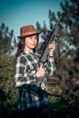 Portrait of a young beautiful girl hunter in a hat and with a hunting rifle in her hands, close-up, soft focus