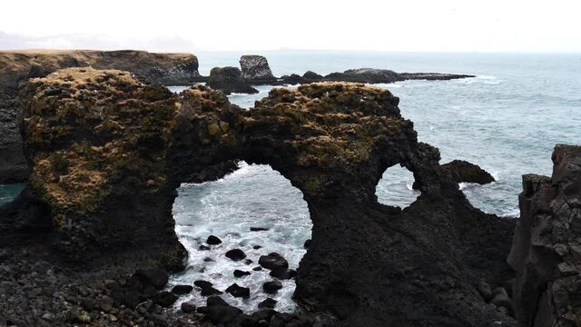View of famous natural arch Gatklettur formed of volcanic basalt rocks on the rough Atlantic coast of Arnarstapi, Sn&aelig;fellsnes, Iceland with surf.