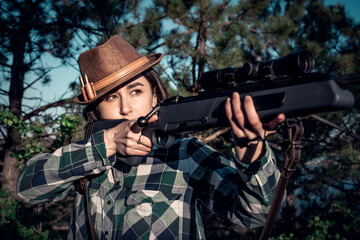 Fototapeta premium Beautiful girl hunter looks into the sight of a bolt rifle, close-up, soft focus
