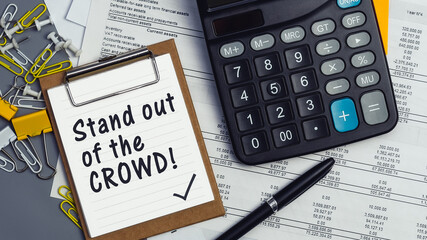 The words Stand out of the crowd written on a white notebook. Work and study concept
