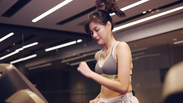 Young beautiful woman asian running on a treadmill at gym. Fitness and healthy lifestyle concept. Side view of girl in sportswear jogging exercise. 