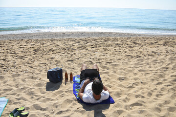 Obraz premium Man drink beer and work on laptop on the beach. Traveler enjoy on send with netbook and cold beer