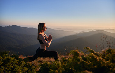 Side view of brunette practicing yoga in Warrior pose. Female is meditating in the mountains after sunset. Concept of fitness.