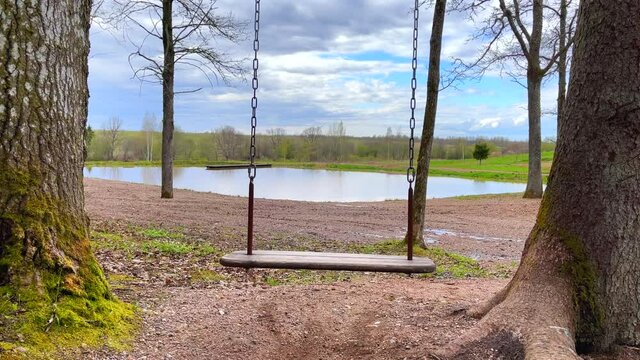 Slightly moving empty wooden swing summer spring outdoor. Sunny day and blue sky. Calmness. No people. 