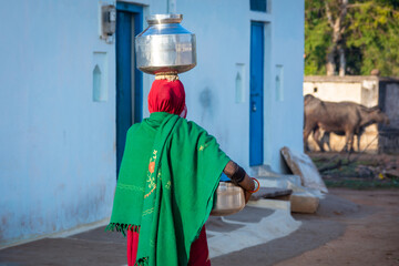 An Indian woman carrying a container of water on her head, An Indian rural scene.