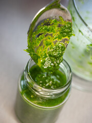 Filling a glass with chopped herbs and fresh pesto. The spoon fills the glass