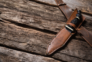Hunting knife and leather case on the old wooden table background. Hunter accessory concept background with copy space.