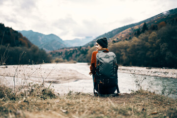 woman traveler with a backpack on her back gestures with her hands and looks at the mountains in the distance