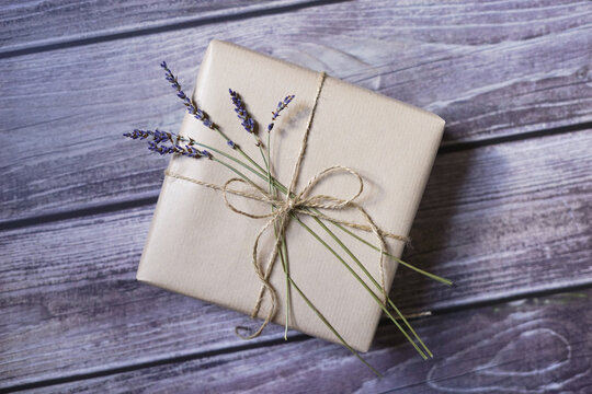 Present wrapped in natural brown paper with lavender flower and twine on wooden background. Natural eco friendly packaging. Zero waste gift wrapping idea.