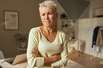 Portrait of displeased disappointed middle aged woman with blonde short hair making grumpy unhappy grimace, crossing arms on her chest feeling bored at home alone. Human emotions and feelings