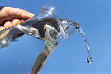 A Clear water flowing from a glass jug on a blue background.