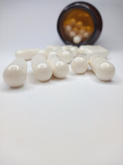 Fototapeta na wymiar scattered white capsules on a white background, behind a brown can