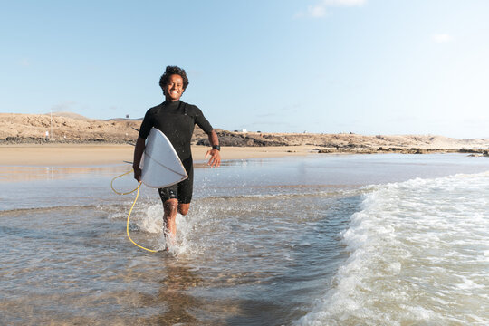 Young happy african malagasy surfer running to the waves at the beach shore. Fun, enjoy, sport concept.