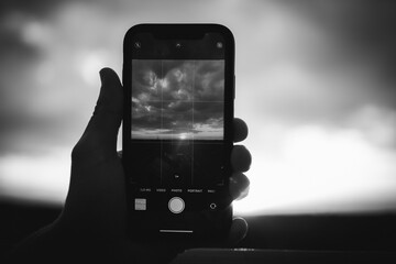 Grayscale shot of a person photographing the sunset with a phone