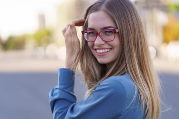 Portrait of carefree young woman smiling and looking at camera with urban background. Cheerful caucasian girl wearing eyeglasses in the city.