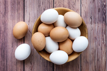 Wooden bowl with brown and white chicken eggs on wood table. Brown and white eggs in bowl on wood background. Free-range organic eggs. Healthy food concept. - Top view
