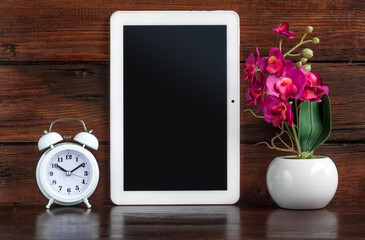 Tablet with Alarm clock and artificial flower decoration on a dark wooden shelf. Clipping path for...