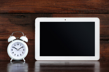 Tablet with Alarm clock on a dark wooden shelf. Clipping path for tablet screen