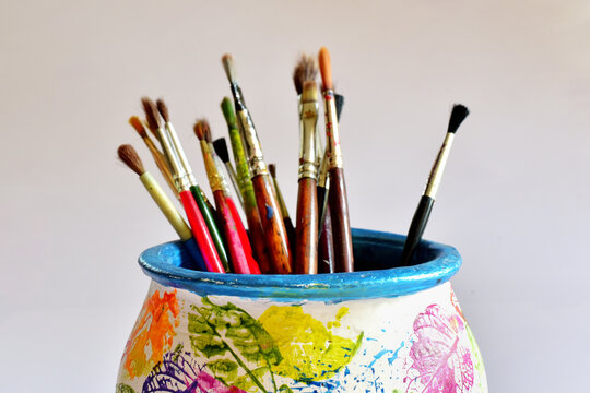 Artist's painting brushes in a painted pot, against white background.