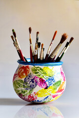 Artist's painting brushes in a painted pot, against white background.