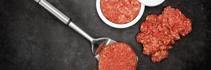 Patty Press with Burgers on Wooden Board on Black Background, Overhead View. Plastic Burger Press and Stuffer With Grill Tools. Beef and Pork Mince Patties.