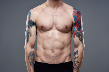 sporty man with pumped up abs tattoos on his arms gray background muscles