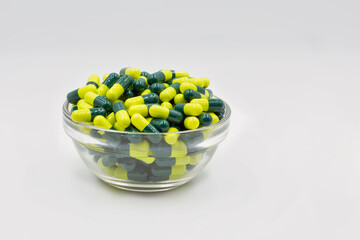 Medical capsules yellow green in glass bowl closeup against white