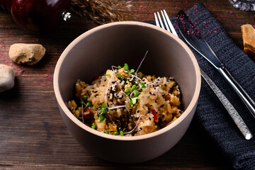 Raw vegan vegetable risotto and microgreens in bowl on rustic wooden background.