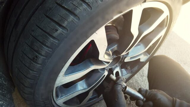 Auto mechanic man with electric screwdriver changing, repairing tire of a car in the car service shop